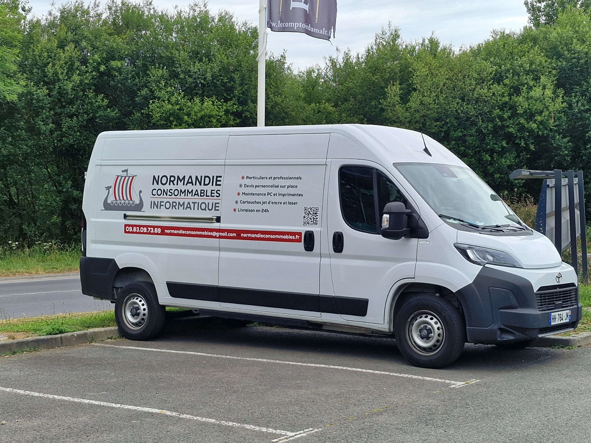 Le camion blanc Normandie Consommables, avec son logo rouge et gris et ses services inscrits sur le flanc.